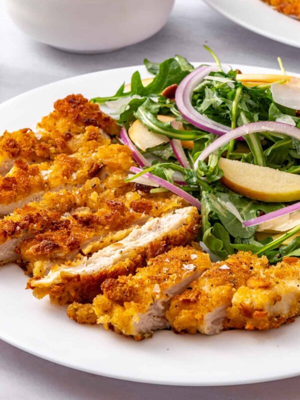 Close-up of crispy chicken cutlets with apple arugula salad and maple Dijon vinaigrette on a white plate.
