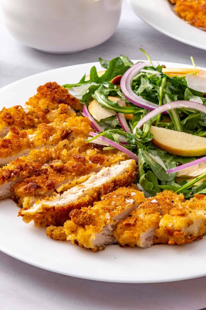 Close-up of crispy chicken cutlets with apple arugula salad and maple Dijon vinaigrette on a white plate.