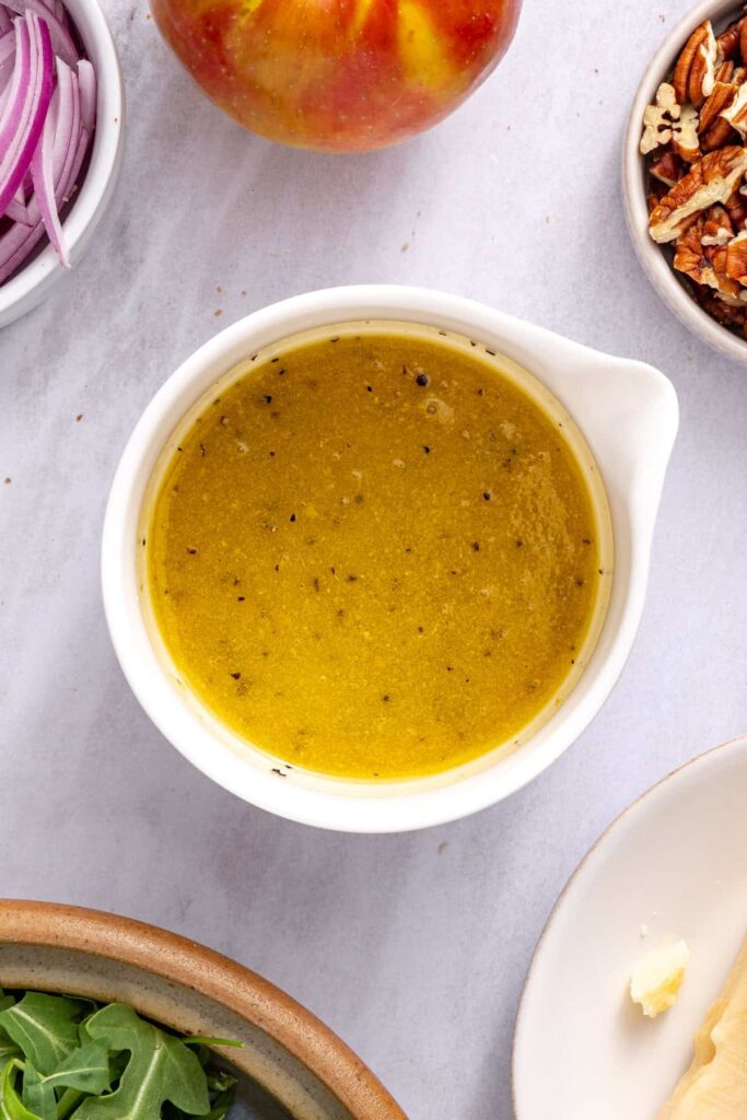 Golden maple Dijon vinaigrette whisked together in a small bowl for apple arugula salad.