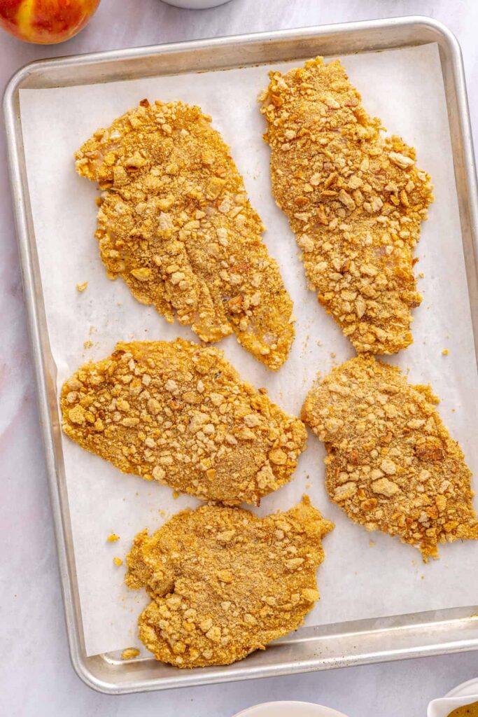 Raw breaded chicken cutlets covered in golden sourdough crumbs, garlic powder, onion powder, and Italian seasoning.