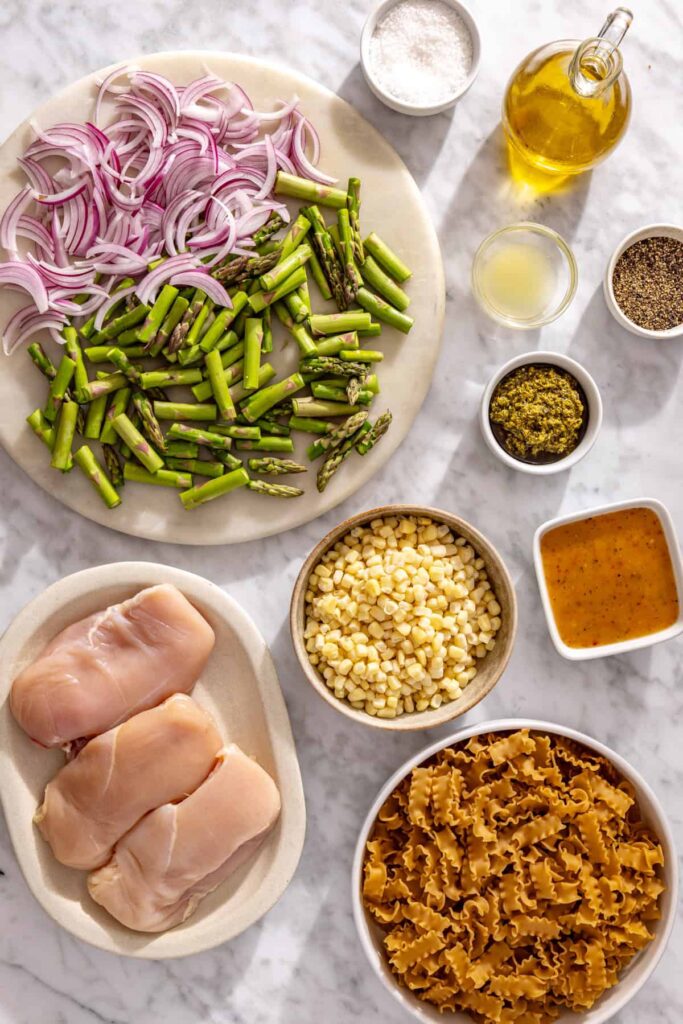 Ingredients for chicken pesto pasta salad including chicken, pasta, corn, asparagus, red onion, pesto, olive oil and Italian vinaigrette