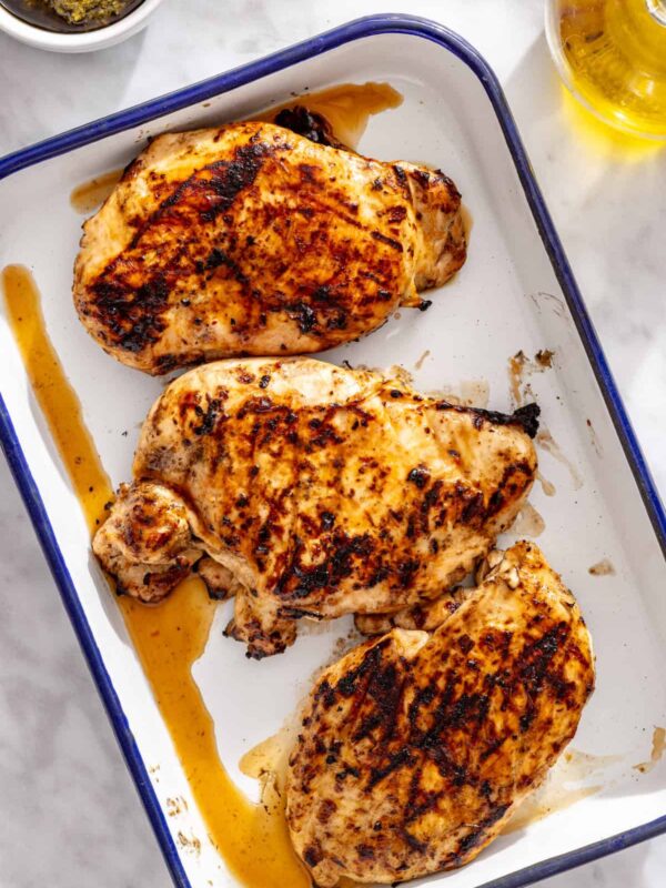 Grilled chicken breasts resting on a tray before slicing