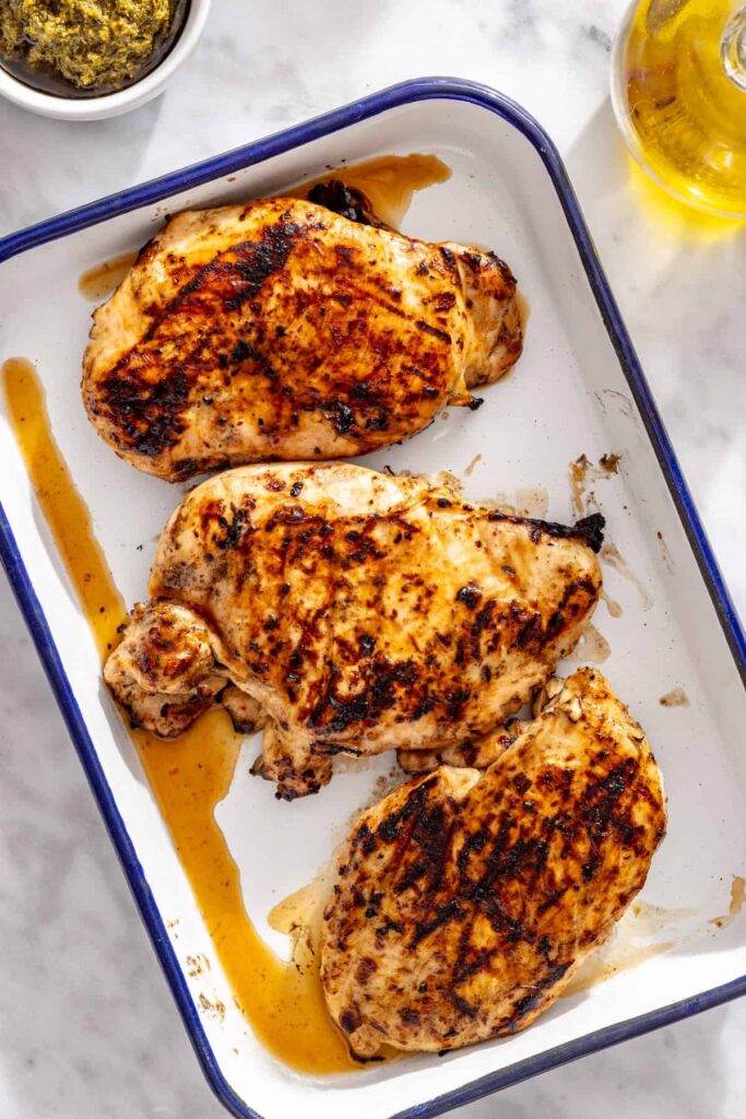 Grilled chicken breasts resting on a tray before slicing