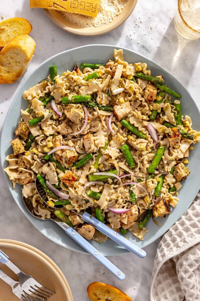 Chicken pesto pasta salad in a large serving bowl with serving spoons