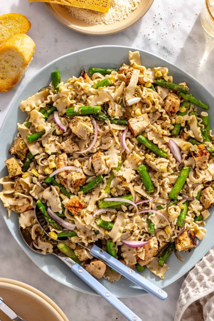Large serving bowl filled with chicken, pasta, grilled vegetables and pesto dressing