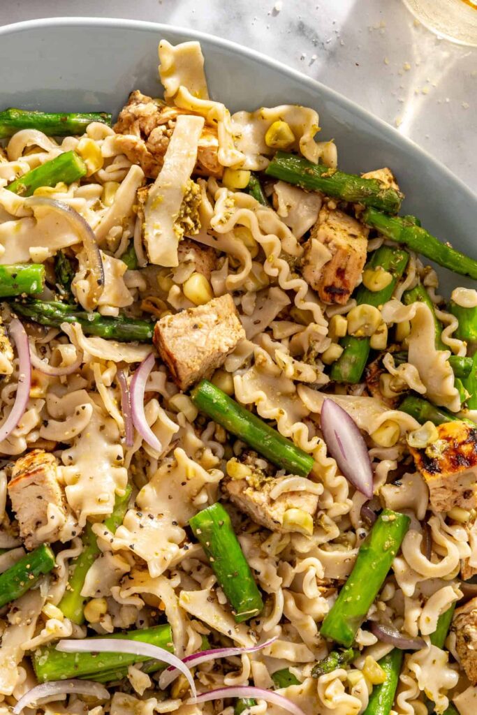 Close-up view of pesto-coated pasta with grilled chicken, asparagus, corn and red onion
