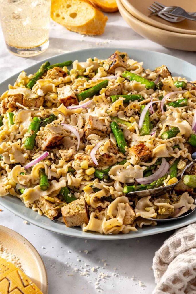 Side view of chicken pesto pasta salad with two serving spoons