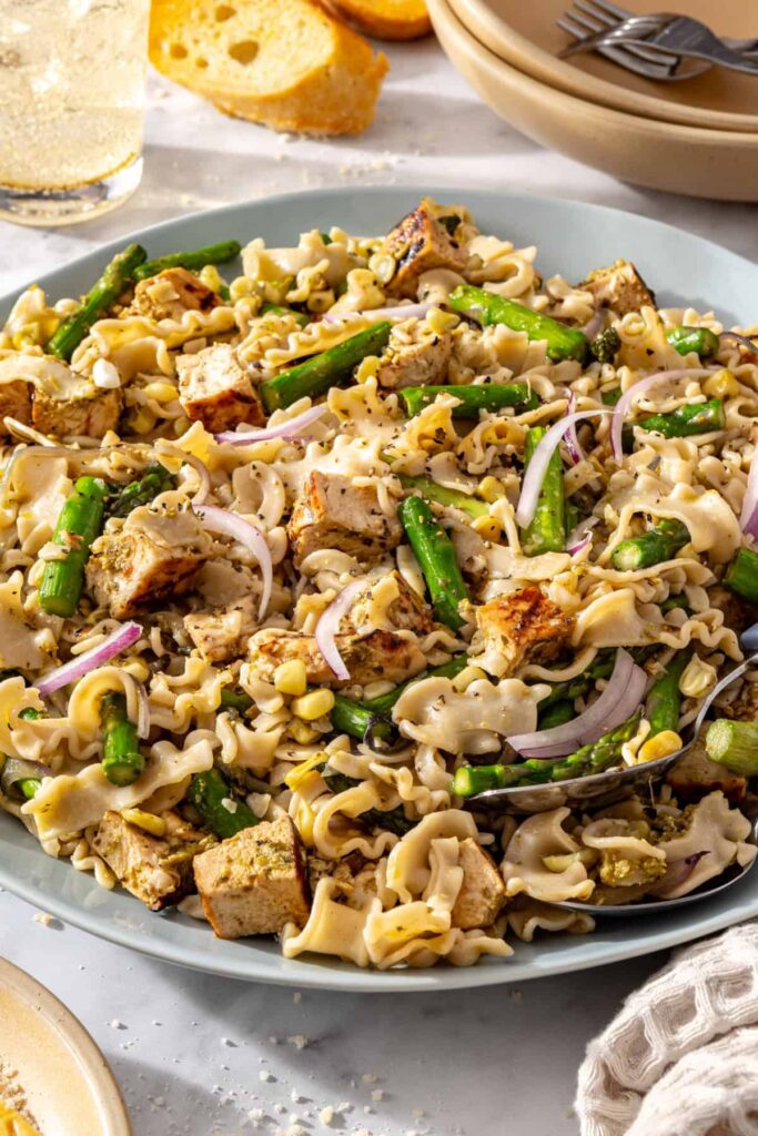 Close-up side view of grilled chicken pesto pasta salad in a serving bowl