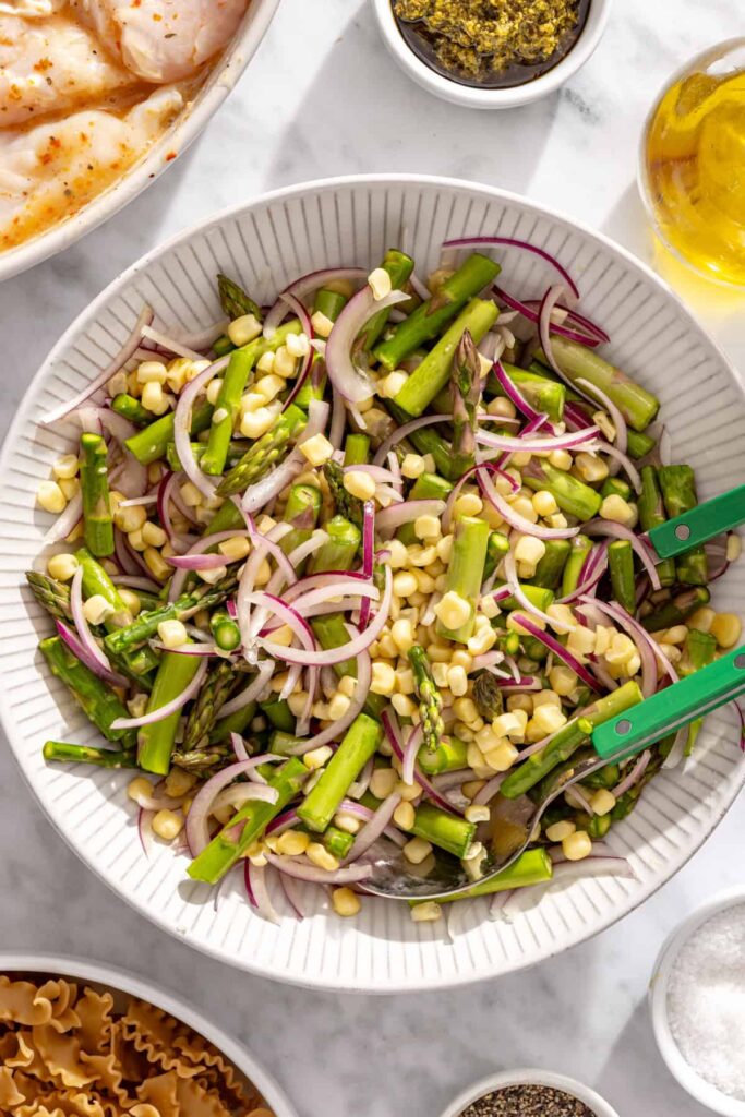 using tongs to toss corn, asparagus and red onion before grilling