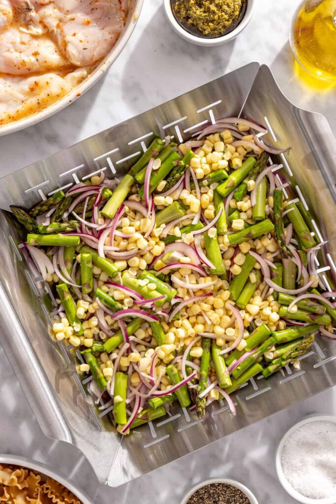 Corn, asparagus and red onion prepared for grilling in a vegetable basket
