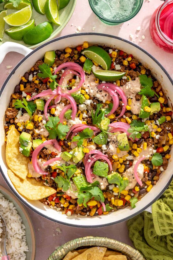 Overhead view of finished street corn taco skillet garnished with cotija, cilantro, lime, and tortilla chips