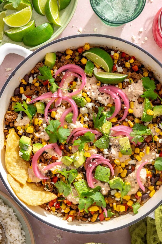 Street corn taco skillet topped with creamy lime cotija sauce, cilantro, lime, and tortilla chips