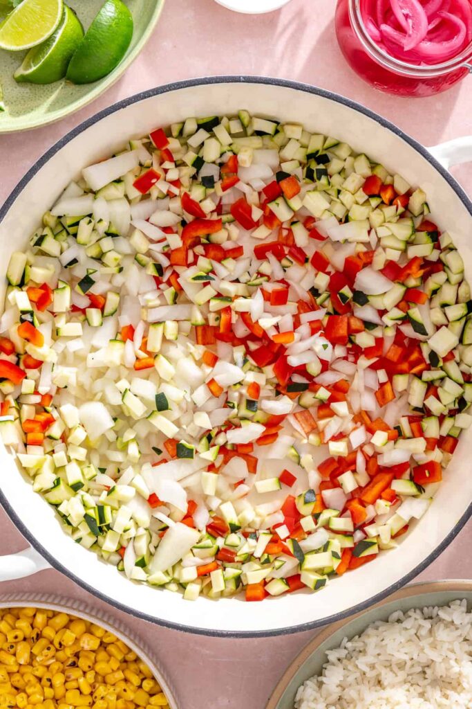 Diced onion, bell pepper, and zucchini cooking in a skillet for street corn taco skillet