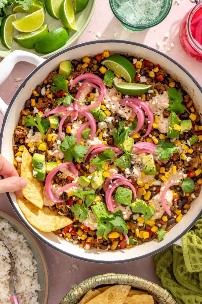 Hand dipping tortilla chips into a finished street corn taco skillet