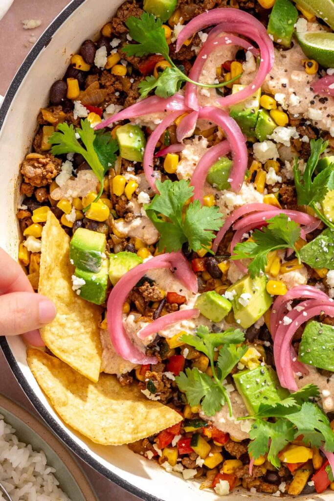 Tortilla chips being dipped into creamy street corn taco skillet