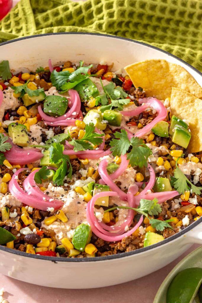 Side view of one-pan taco skillet topped with creamy lime cotija sauce and fresh garnishes