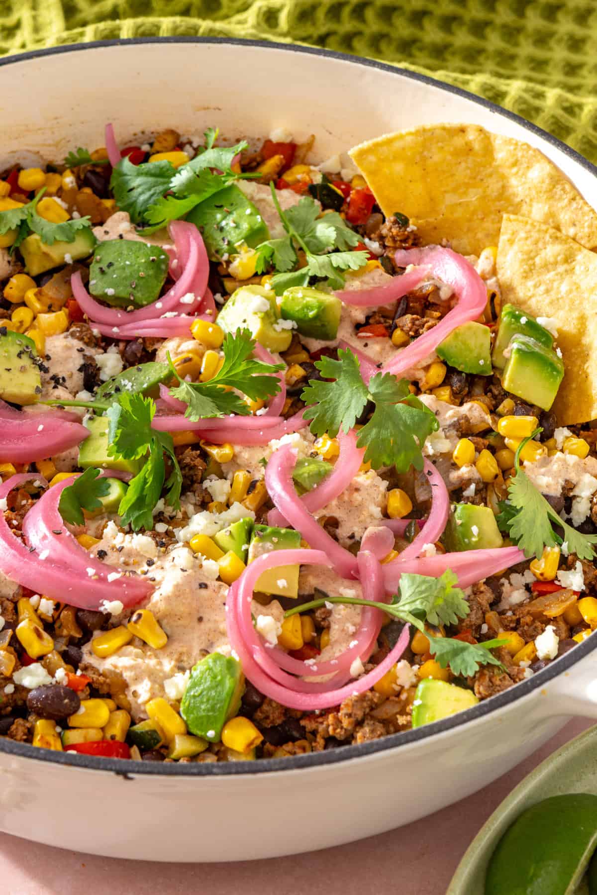 Close-up side angle of street corn taco skillet with tortilla chips dipping into the skillet, topped with pickled red onions, cotija, cilantro, and lime