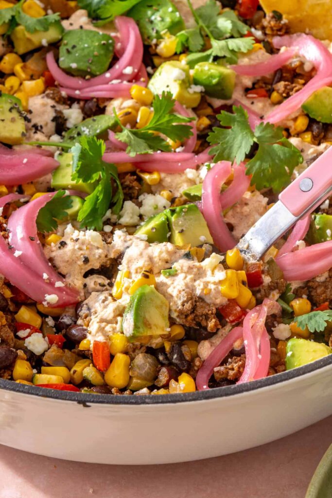 Close-up of street corn taco skillet showing seasoned beef, black beans, fire-roasted corn, vegetables, and creamy cotija sauce