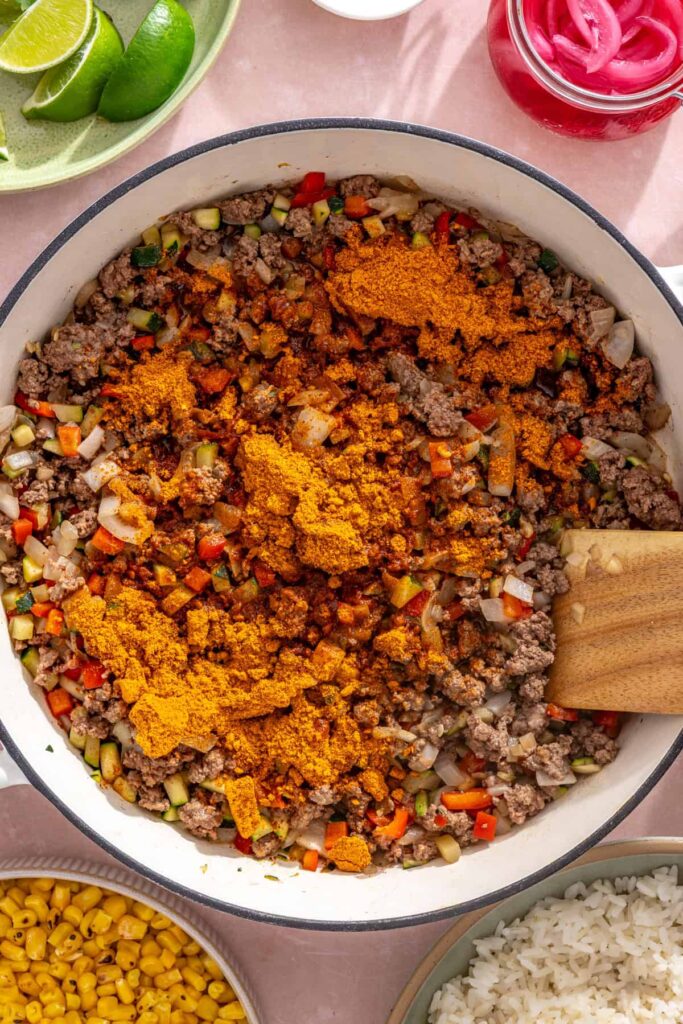 Taco seasoning and water added to browned beef and vegetables in the skillet