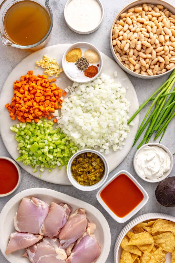 Ingredients for Instant Pot buffalo chicken chili including chicken thighs, cannellini beans, vegetables, green chiles and buffalo sauce