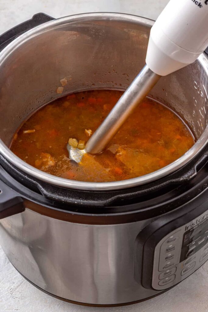 Immersion blender partially blending Instant Pot buffalo chicken chili until creamy
