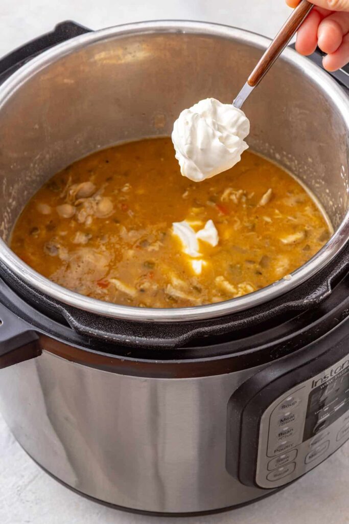 Greek yogurt being stirred into buffalo chicken chili for a creamy finish