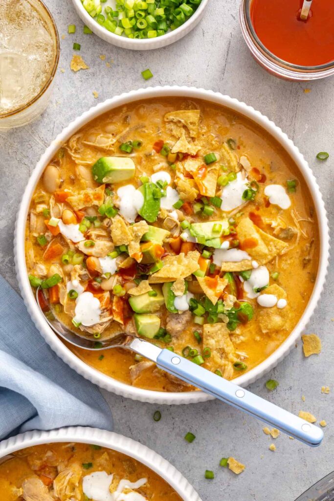 Overhead bowl of buffalo chicken chili topped with avocado, green onion, ranch and buffalo sauce