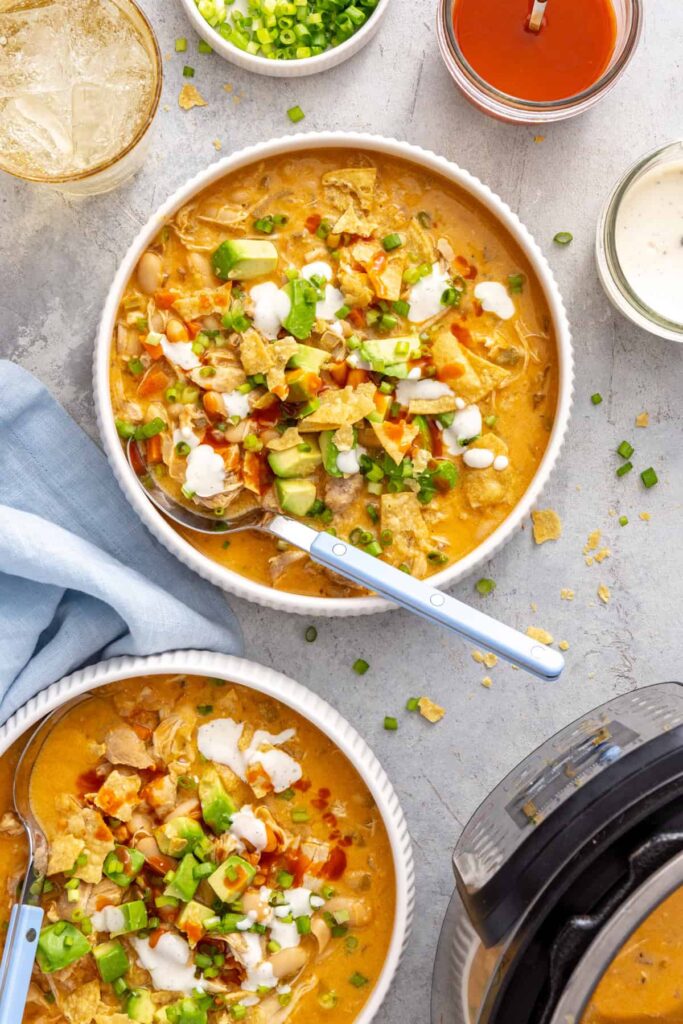Overhead bowl of creamy buffalo chicken chili served with a spoon and extra buffalo sauce