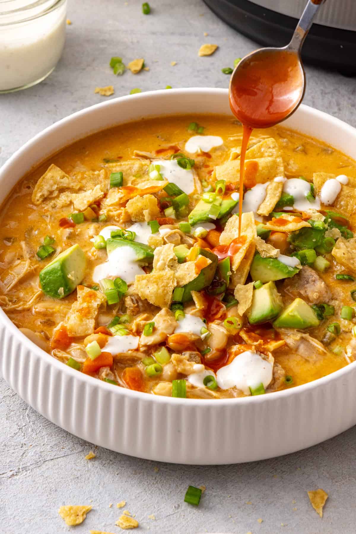 Instant Pot buffalo chicken chili topped with avocado, green onion and ranch with buffalo sauce drizzled over top
