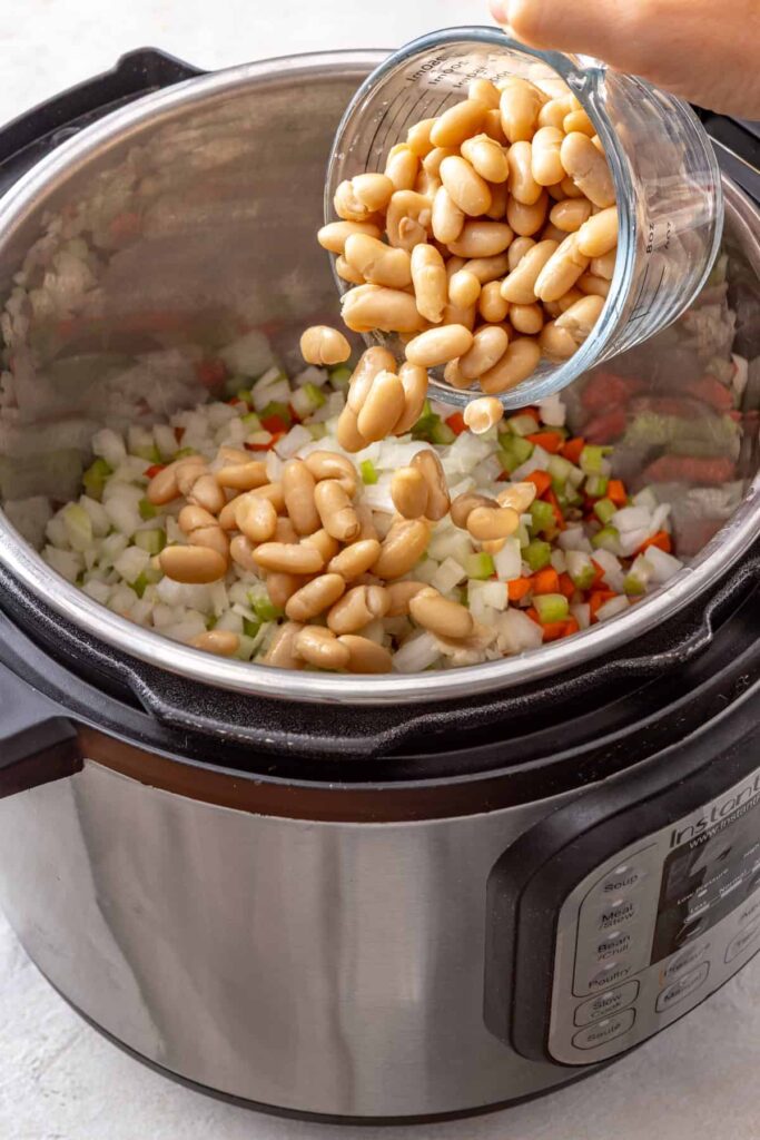 pouring beans into an Instant Pot with chicken thighs and vegetables for buffalo chicken chili