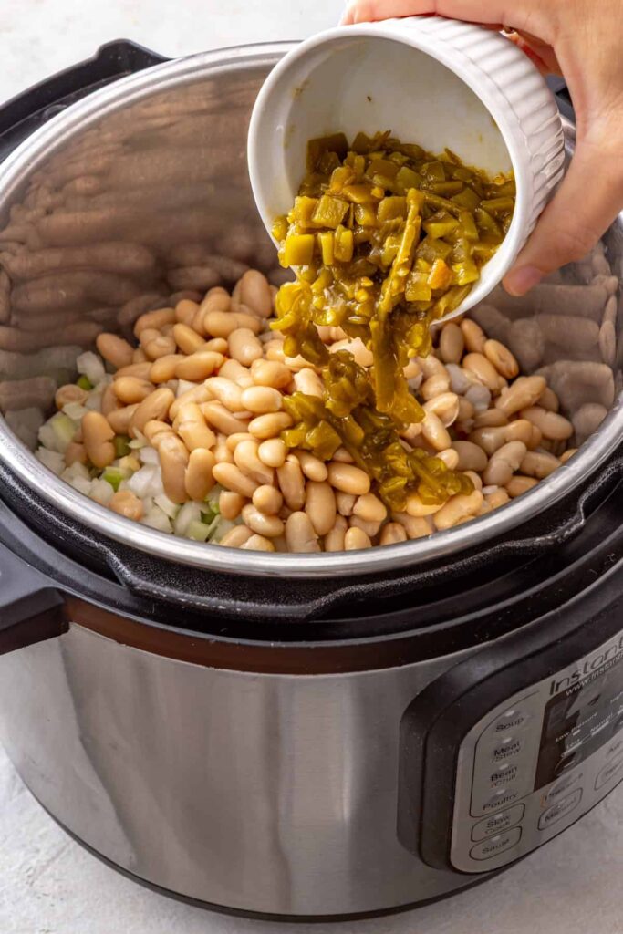 green chiles being poured into the Instant Pot as part of a buffalo chicken chili recipe