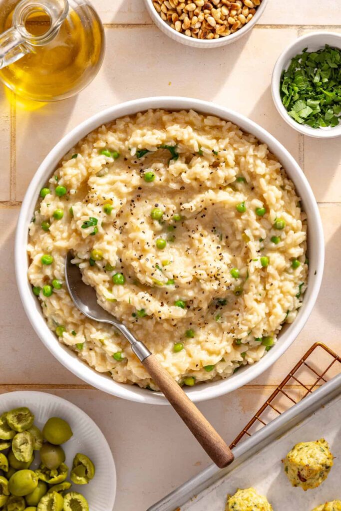 Creamy lemon parmesan rice in a bowl with toasted pine nuts, olives and fresh parsley