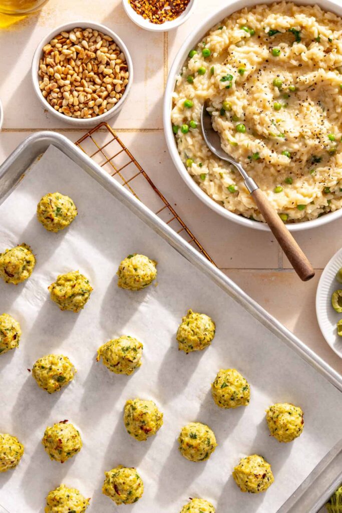 Golden lemon artichoke chicken meatballs cooling beside a bowl of creamy parmesan rice