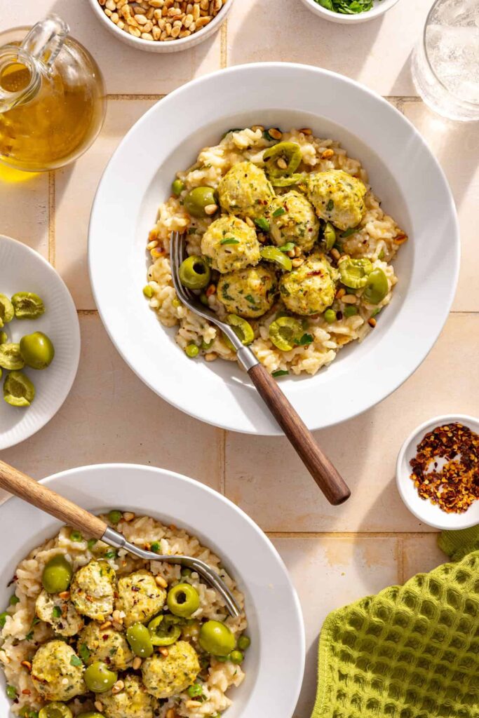 Two bowls of lemon artichoke chicken meatballs served over creamy parmesan rice with herbs and toasted pine nuts
