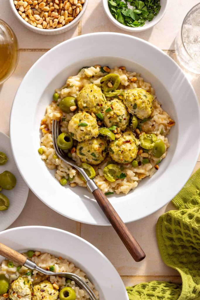 Close-up bowl of lemon artichoke chicken meatballs served over creamy parmesan rice with fresh herbs