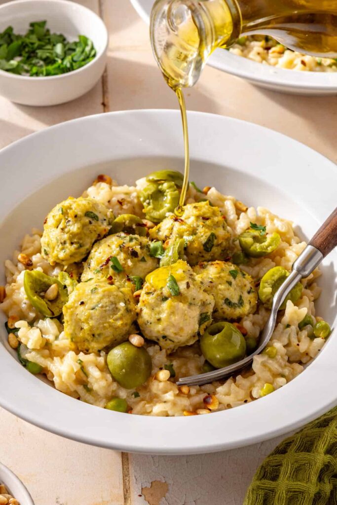 Close-up of lemon artichoke chicken meatballs over creamy parmesan rice with olive oil drizzled on top