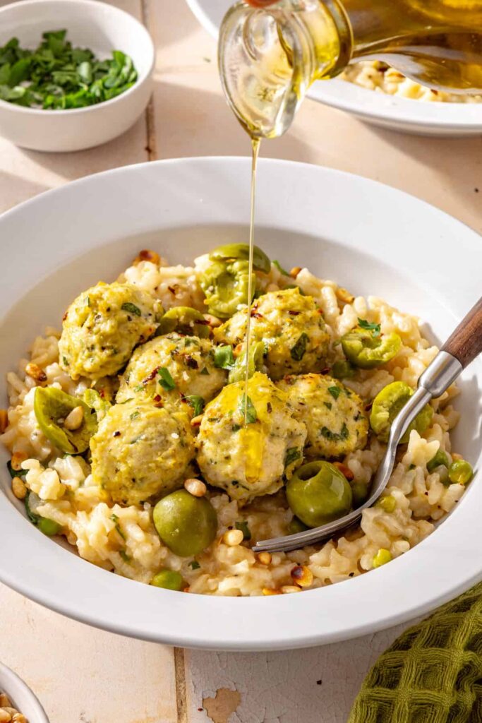 Olive oil drizzled over lemon artichoke chicken meatballs and creamy parmesan rice