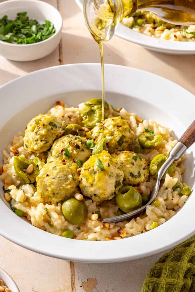 Lemon artichoke chicken meatballs served over creamy parmesan rice with Castelvetrano olives and olive oil drizzled on top