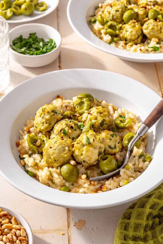 Side view of lemon artichoke chicken meatballs served over creamy parmesan rice at a dinner table