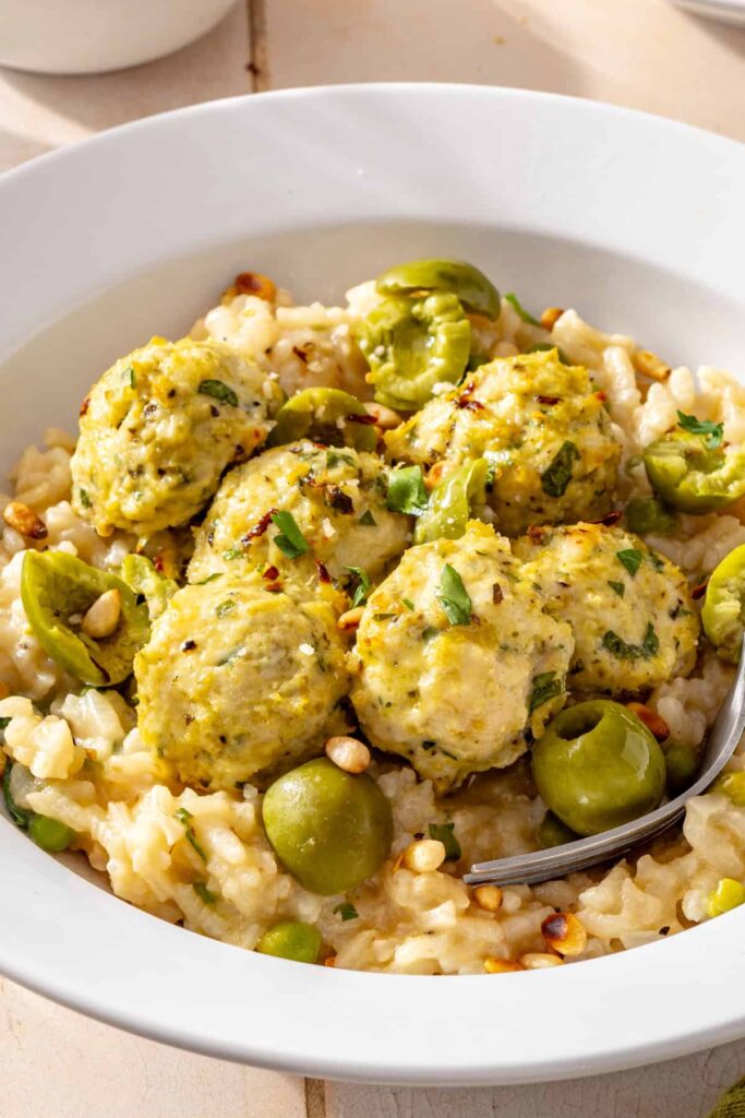 Detailed close-up of lemon artichoke meatballs over creamy lemon parmesan rice with fresh herbs