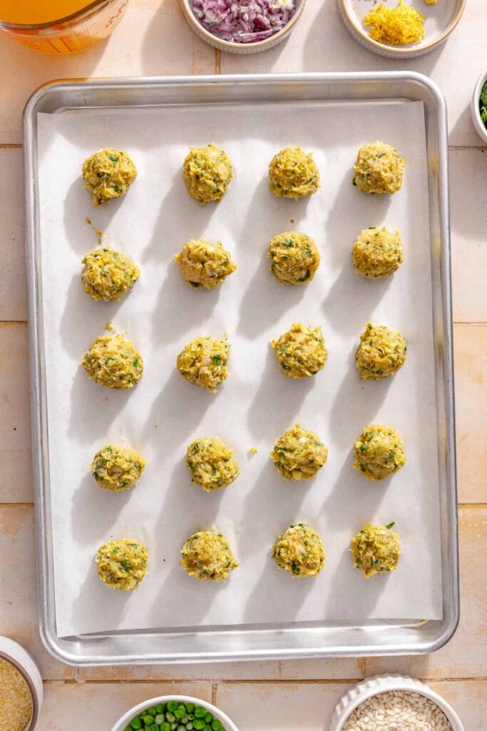 Lemon artichoke chicken meatballs arranged on a parchment-lined baking sheet