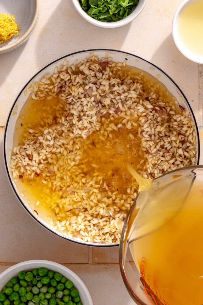 Warm bone broth being poured into arborio rice for creamy parmesan rice