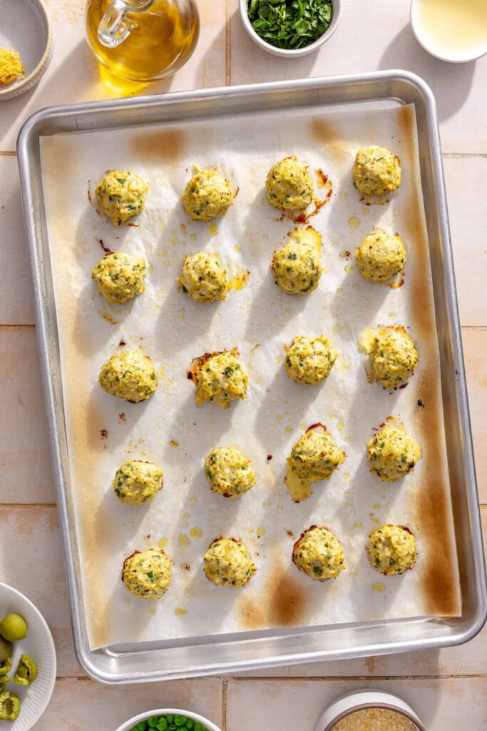 Baked lemon artichoke chicken meatballs on a parchment-lined baking sheet