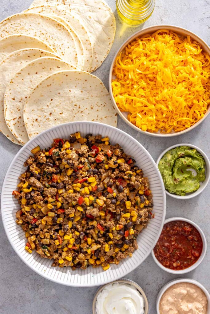 Ingredients for easy sheet pan quesadillas with tortillas, leftover street corn taco filling, cheddar cheese and avocado oil