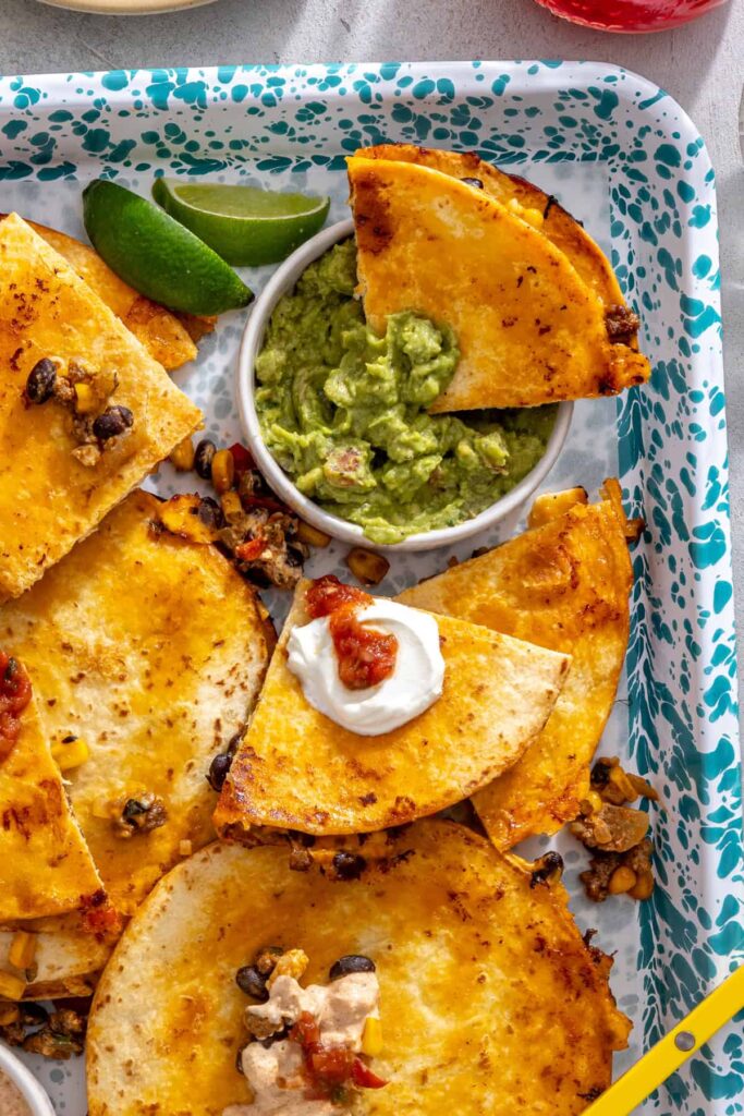 Sheet pan quesadilla wedge dipped into guacamole with crispy wedges on a serving tray