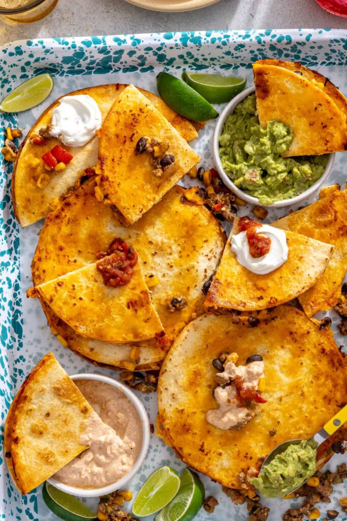 Crispy baked quesadilla wedges served on a splatter tray with guacamole and lime