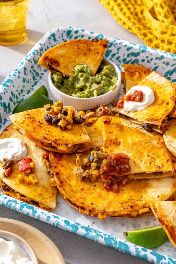 Crispy sheet pan quesadillas served on a tray with guacamole, lime and dipping sauces