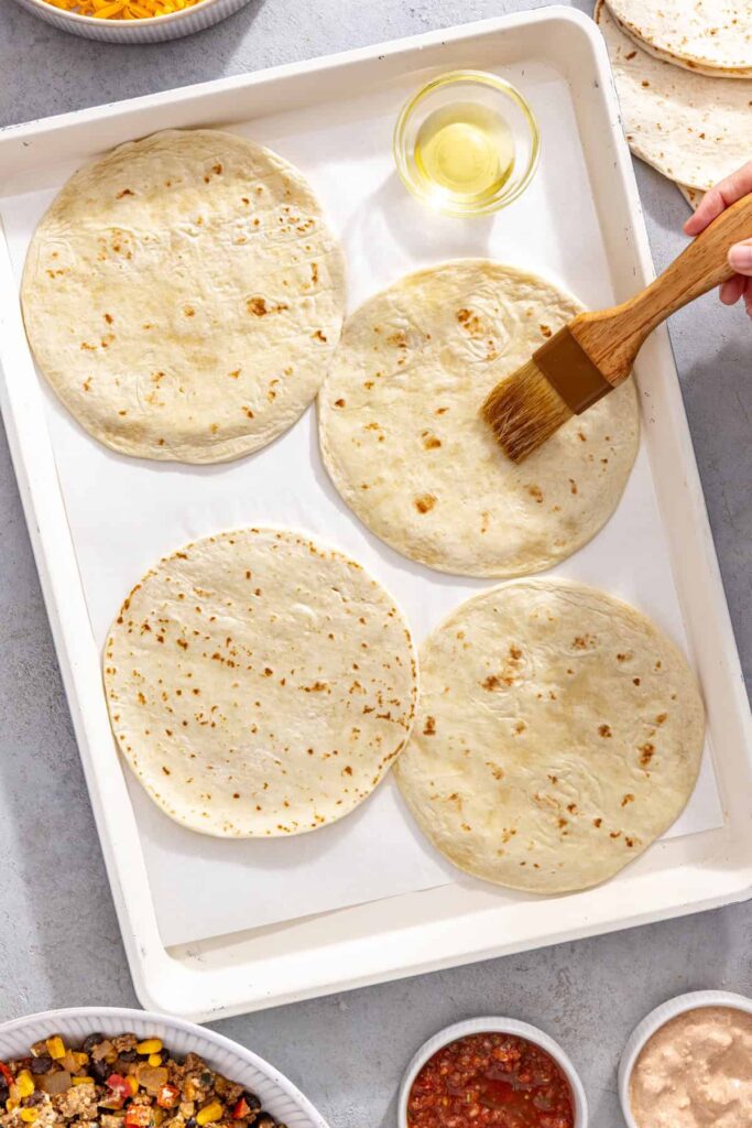Tortillas brushed with avocado oil and flipped onto a parchment-lined sheet pan