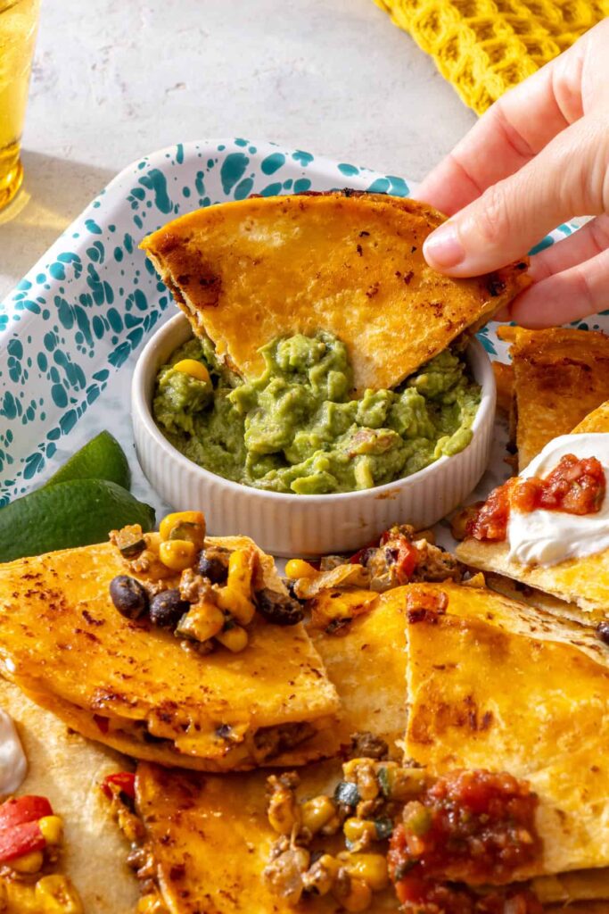 Hand dipping a golden sheet pan quesadilla into creamy guacamole
