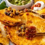 Sheet pan quesadilla wedge dipped into guacamole with crispy quesadilla wedges, salsa, Greek yogurt and lime